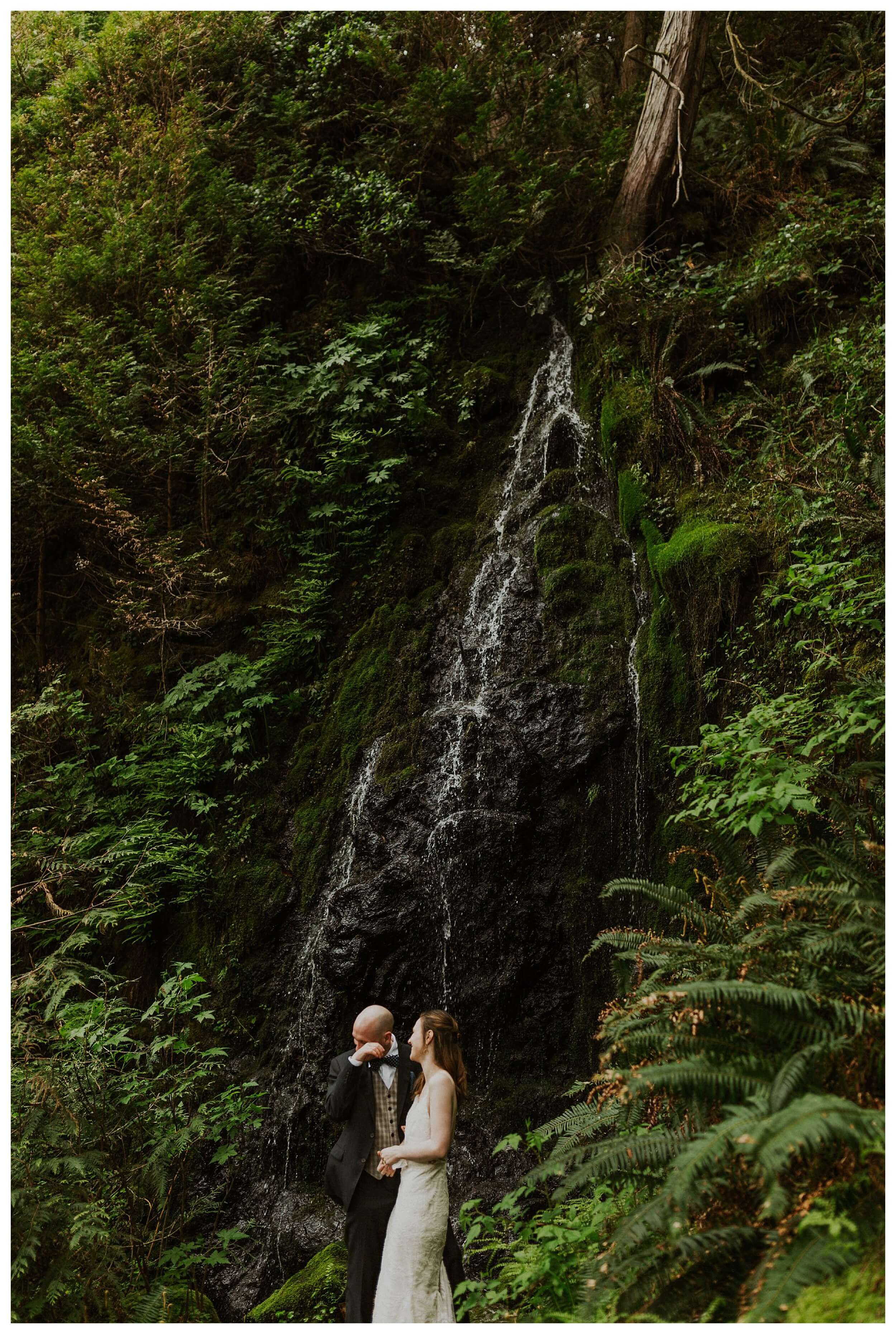 bride and groom standing at waterfall landscape